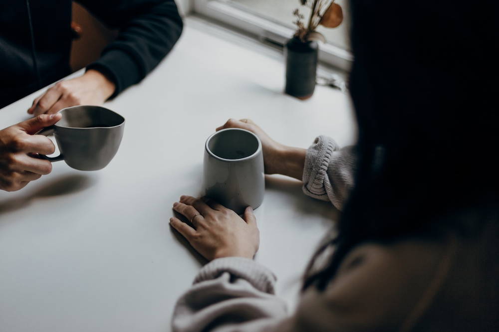 Two people at a table with mugs, mid conversation, seen from above