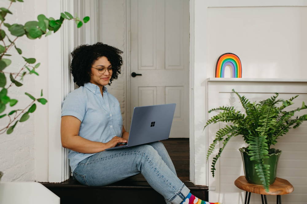 A woman sitting on a step at home, laptop on her knees, mid video call